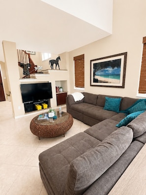 Ein Wohnzimmer mit einem Ecksofa, einem Flachbildfernseher, einem Kamin und einem gerahmten Strandbild.