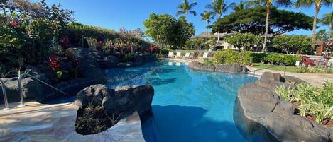 A pool with a rock feature, clear blue water, and a tropical garden setting.