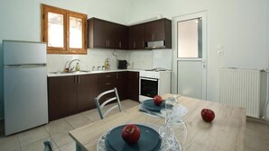 A compact kitchen with dark cabinets, a white refrigerator, a stove, and a dining table with plates and glasses.