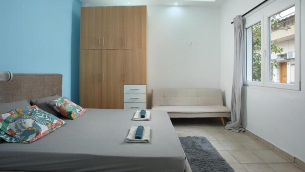 A bedroom with a bed, a sofa, a wardrobe, and a window with curtains.