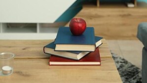A living room with a flat-screen TV, a coffee table with books and an apple, and a blue wall.