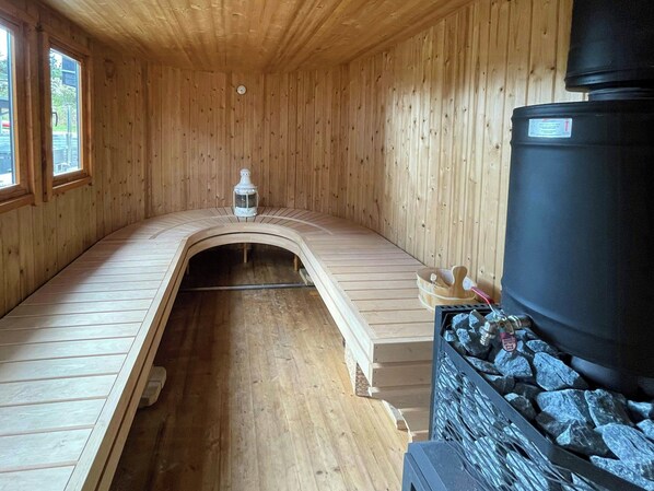 Ein Saunaraum mit Holzwänden, einer Bank, einer Wärmequelle und einem mit Steinen gefüllten Behälter.