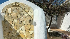 A stone wall with a metal door, white walls, and a tree in the background. - Design rustic villa in Alcaucín with pool (29713, Málaga)