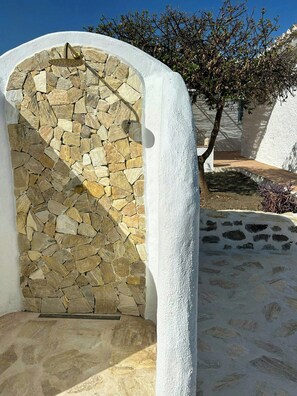 A stone wall with a metal door, white walls, and a tree in the background. - Design rustic villa in Alcaucín with pool (29713, Málaga)