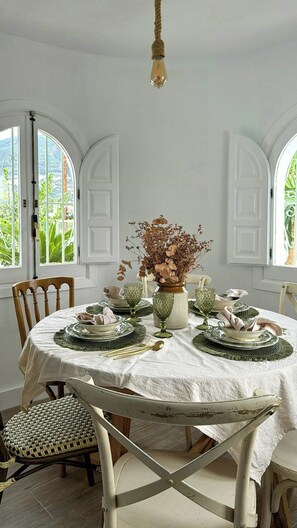A dining room with a round table, white chairs, and a vase with dried flowers. - Design rustic villa in Alcaucín with pool (29713, Málaga)