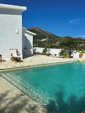 A pool with clear water, a white building, and a mountain in the background. - Design rustic villa in Alcaucín with pool (29713, Málaga)