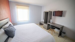 Een slaapkamer met een bed, een bureau, een stoel, een televisie en een raam.