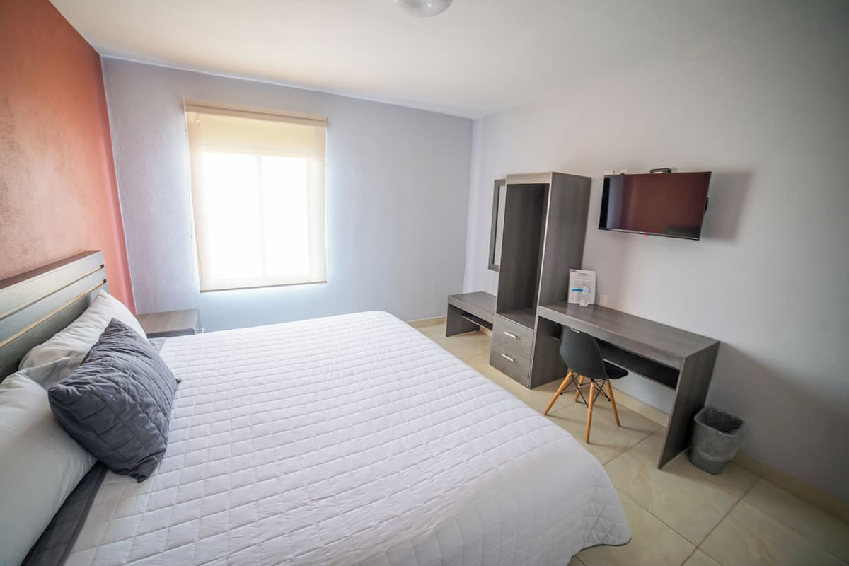 Un dormitorio con cama, escritorio, silla, televisor y ventana.