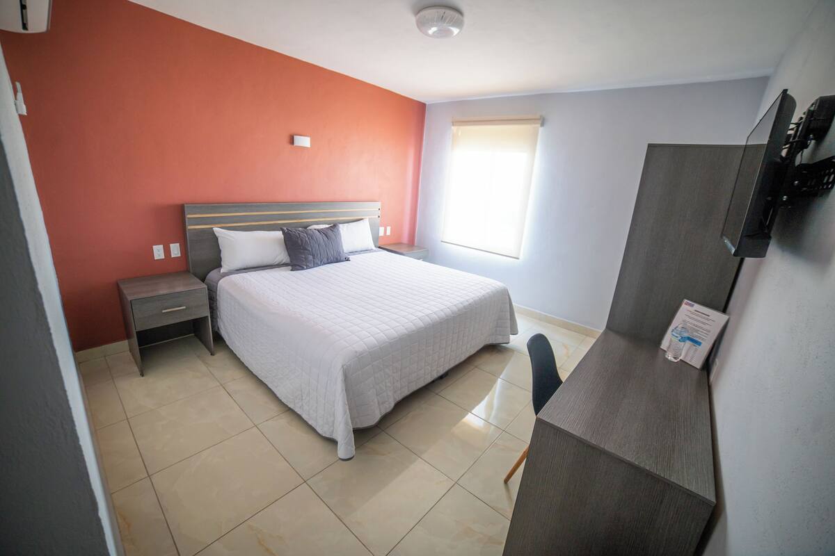 Una habitación de hotel con cama, mesita de noche, escritorio y televisión.
