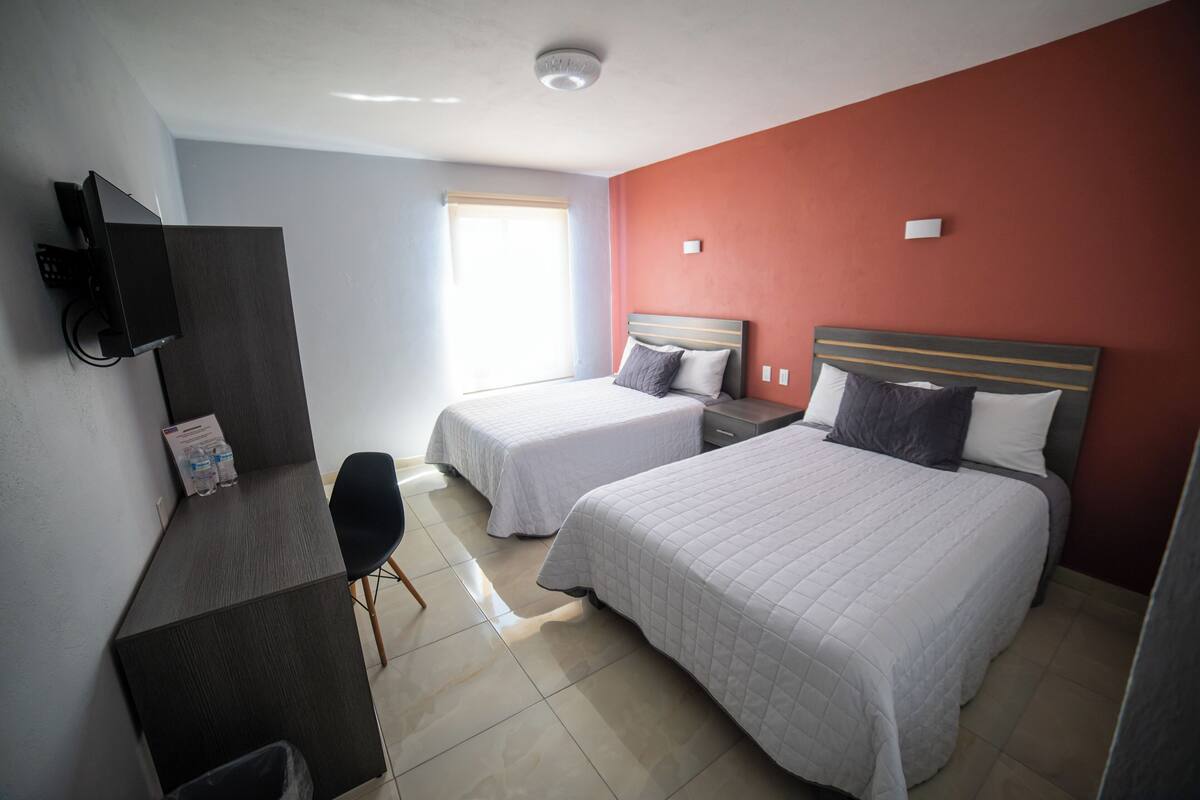 Habitación de hotel con dos camas, un escritorio, una silla, un televisor y una ventana con persianas.