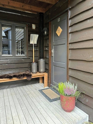 Eingang eines Holzchalets mit einer Bank, einer Tür mit Nummernschild und einem Blumentopf.