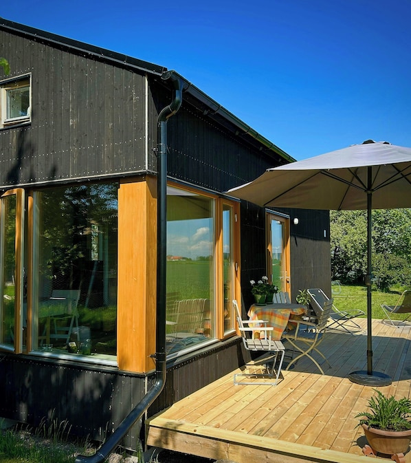 A modern house with large windows, a deck with outdoor furniture, and a patio umbrella.