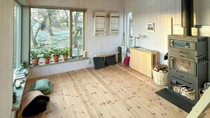Een ruime kamer met houten vloeren, grote ramen, een ingebouwde houtkachel en een bankje bij de ramen.