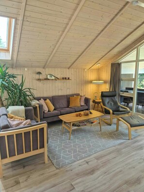 A cozy room with a wooden ceiling, a sofa, a chair, a coffee table, and a large window.