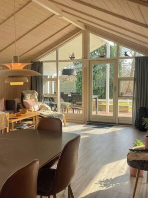A spacious room with a large dining table, comfortable seating, and a view through large glass doors to an outdoor area. - Summer house near beach and nature (Væggerløse)