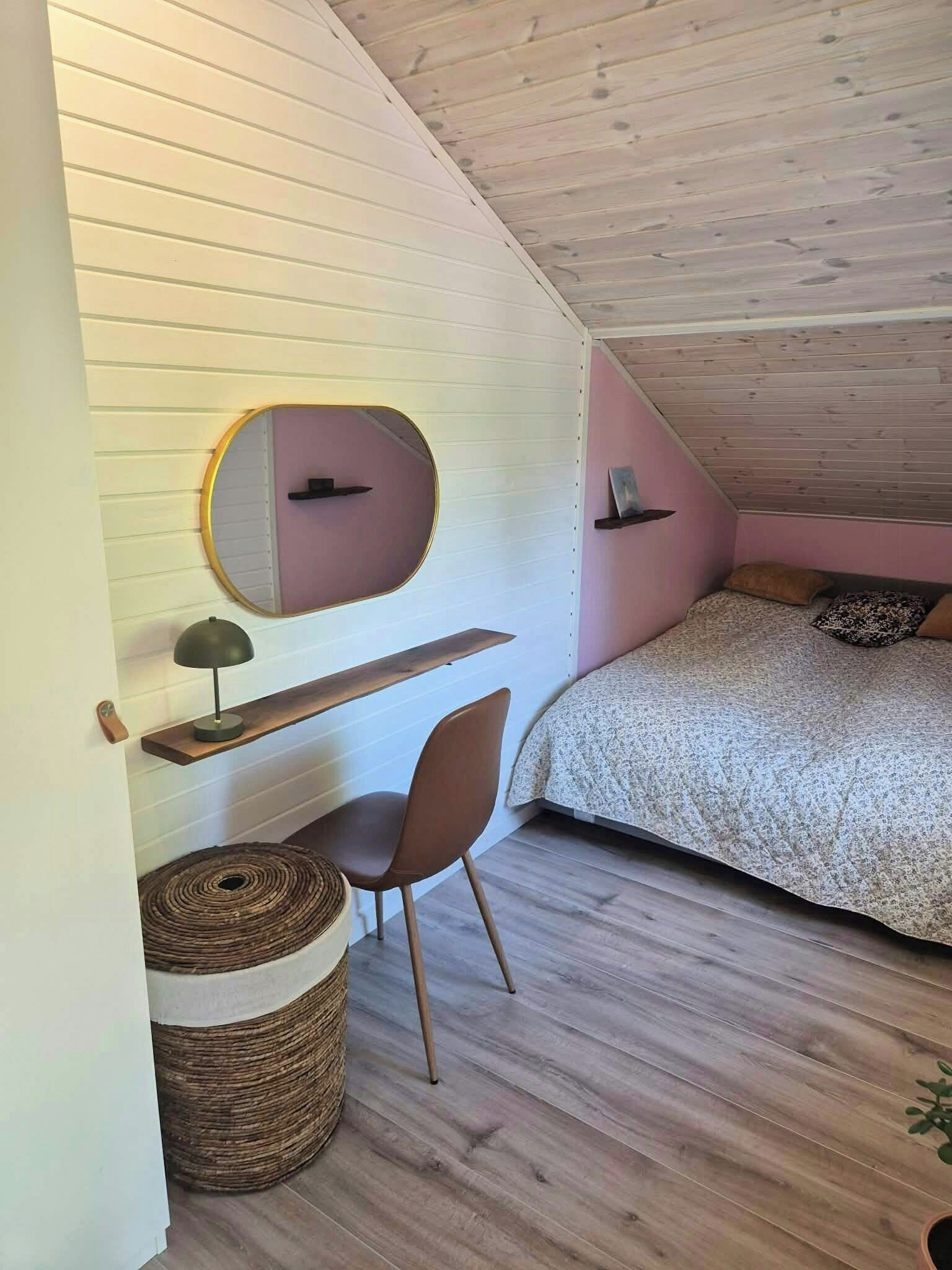 Ein Schlafzimmer mit schrägverdeckter Decke, einem Bett, einem Schreibtisch mit Stuhl, einem runden Spiegel und einem kleinen runden Teppich.