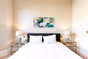 Ein Hotelzimmer mit einem großen Bett, zwei Nachttischen mit Lampen, einem modernen Wandbild und einem dunklen Kopfteil.