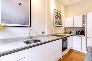 Eine moderne Küche mit weißen Schränken, einer Edelstahl-Spüle, einem eingebauten Backofen und einer Mikrowelle.