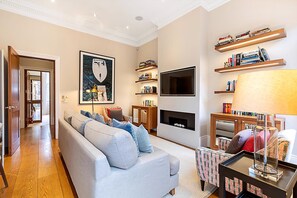 Ein Wohnzimmer mit einer Couch, einem Kamin, Bücherregalen, einem Fernseher und einem gerahmten Bild an der Wand.