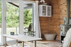 A wooden cabin interior with a table, chairs, a cabinet, a basket, and a fireplace. - Simple life in traditional home by Lyngså Beach (Sæby)