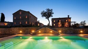 Un edificio de piedra grande con una piscina delantera, rodeado de muros de piedra y un árbol.