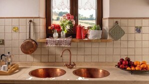 A kitchen with two copper sinks, wooden cabinets, a window with a view, and a hanging pot rack. - Historic villa with pool in Marche hills (Sant'Angelo in Pontano)