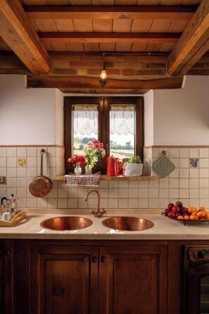 Eine Küche mit zwei Messing-Spülen, Holzschränken, einem Fenster mit Blick und einem hängenden Topfhalter.