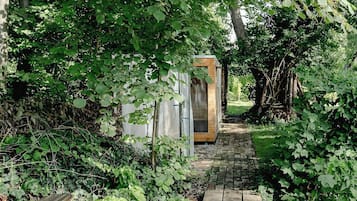 A wooden pathway leading to a small wooden structure, surrounded by dense green foliage.