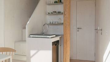 A compact kitchen with a sink, wooden chair, and a staircase leading to an upper level.