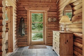 Ein rustikaler Innenraum einer Blockhütte mit Holztür, Steinfußboden, Kommode und Spiegel.