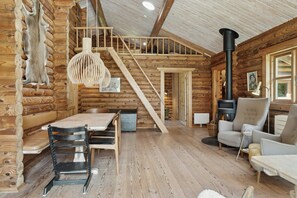 Ein Holzblockhaus-Innenraum mit Esstisch, Stühlen, einer Couch, einem Kamin und einer Treppe.