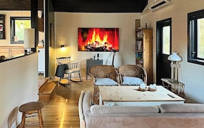 Ein gemütliches Wohnzimmer mit Kamin, Korbmöbeln und Blick zur Küche.