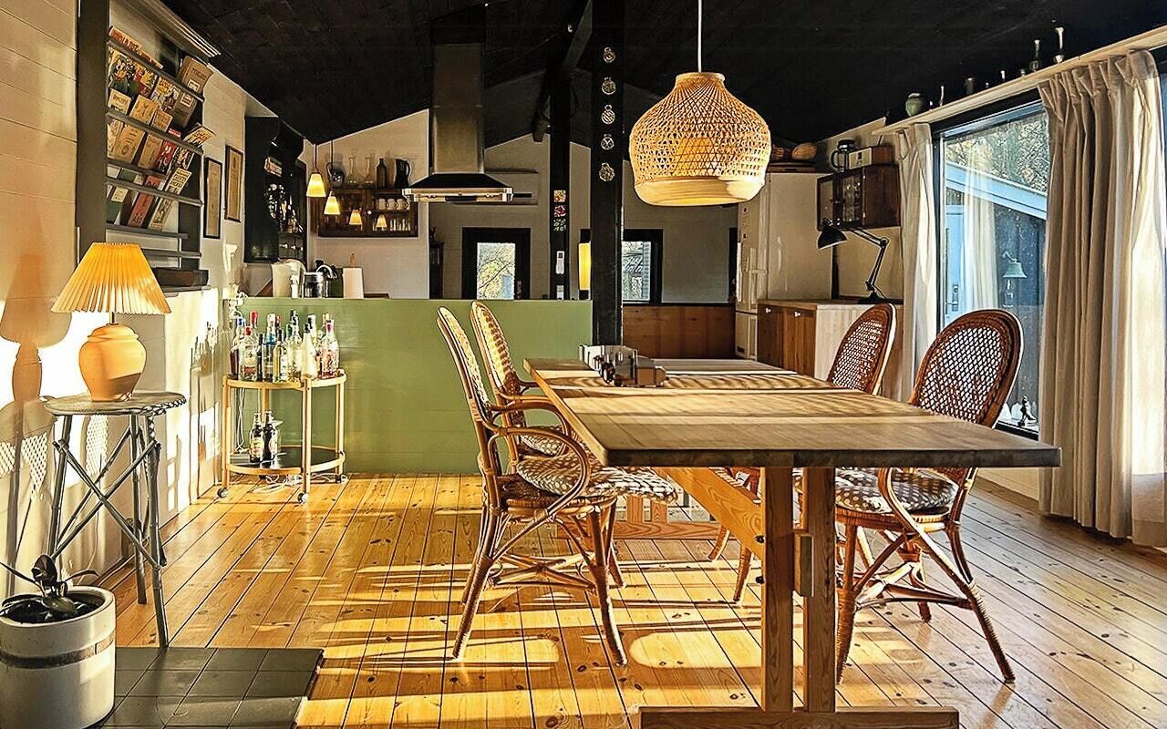A dining area with a long wooden table, wicker chairs, and a hanging light fixture.