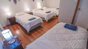 A hotel room with three beds, a nightstand with a lamp, and a wooden floor.
