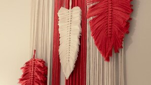 Eine Wand mit drei Wandbehängen aus Makramee in Rot und Weiß.
