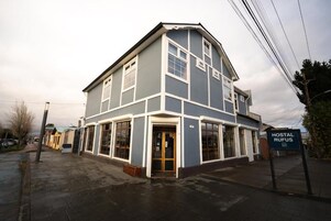 Un edificio de dos pisos con techo plano, ventanas amplias y un letrero que indica que es un albergue.