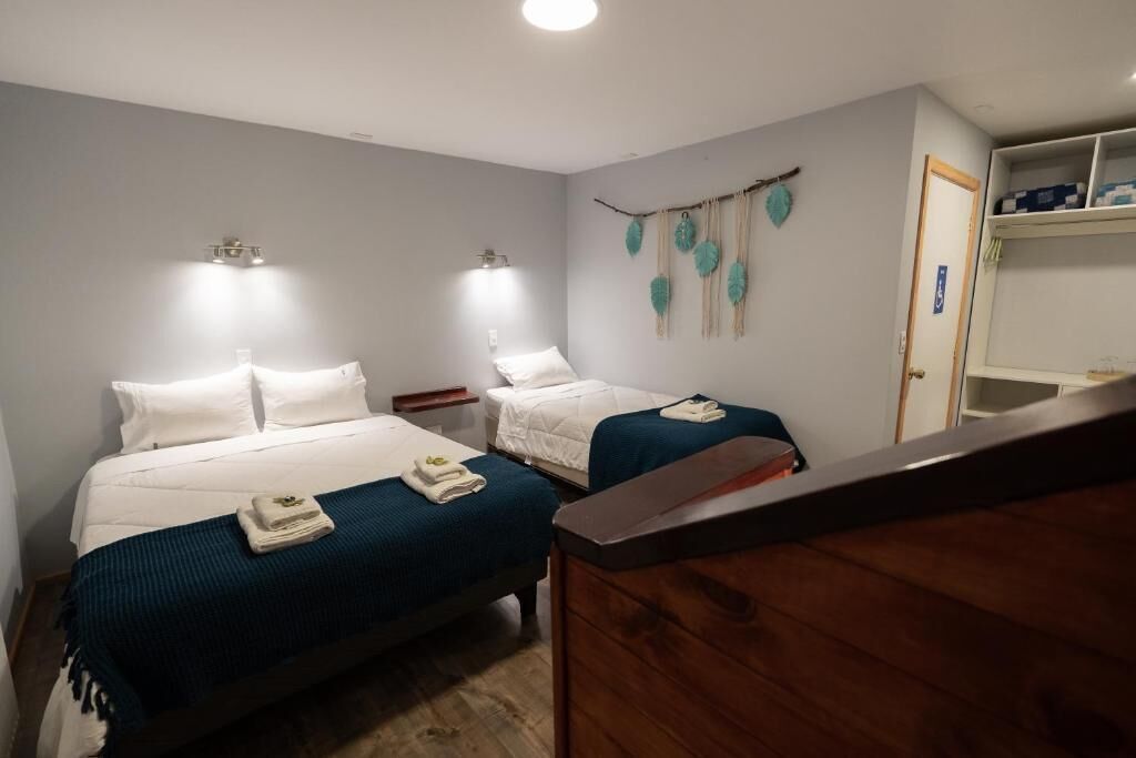 Une chambre avec deux lits, une commode en bois, une étagère avec des boîtes et un élément décoratif fixé au mur.