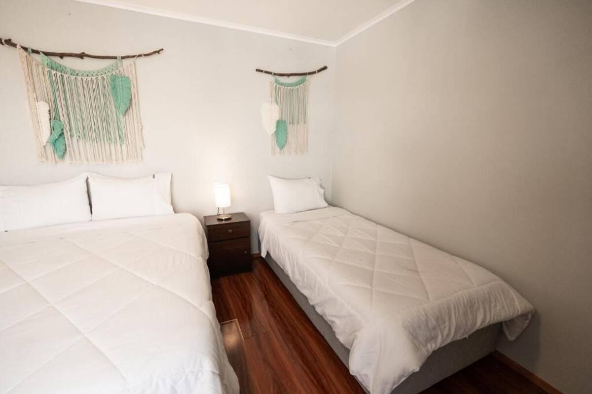 A room with two beds, a nightstand, and macramé wall hangings.