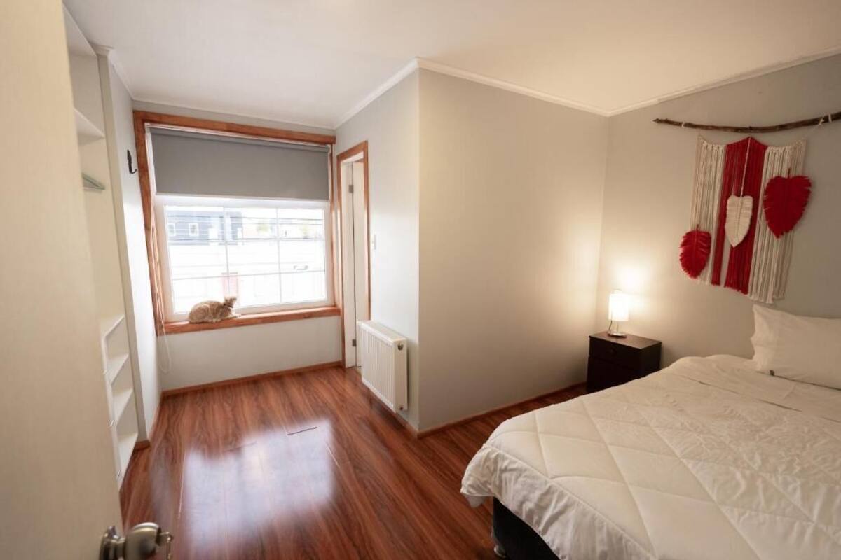 A bedroom with a bed, a window with a view, a radiator, and a nightstand with a lamp.