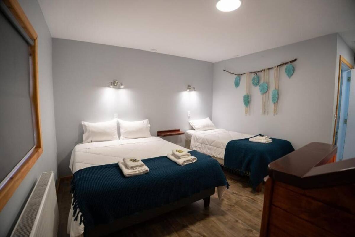 A hotel room with two beds, a dresser, and a wall-mounted shelf.