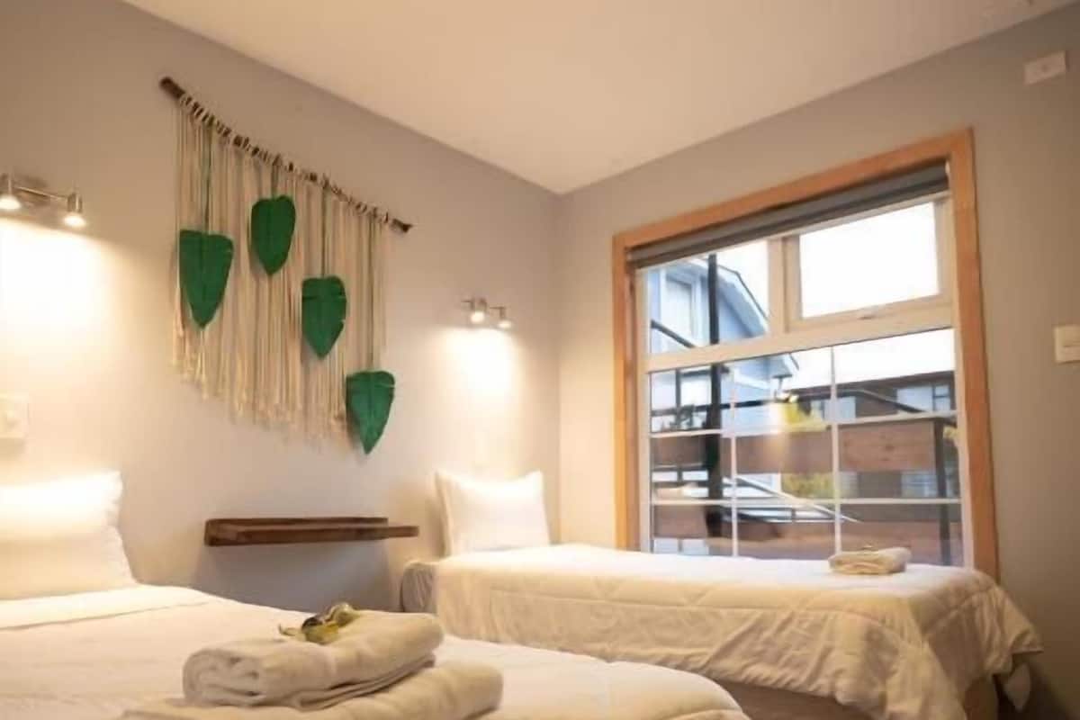 A hotel room with two beds, a window with blinds, and a wall-mounted light fixture.