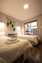 Habitación de hotel con dos camas, una ventana con persianas y una lámpara fijada a la pared.