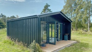 A small, dark-colored cabin with a glass door and a wooden deck. - Charming holiday home near the beach (Gedser)