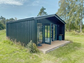 A small, dark-colored cabin with a glass door and a wooden deck. - Charming holiday home near the beach (Gedser)