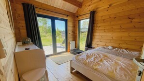 A wooden cabin room with a bed, a desk, and a view of the outdoors. - Charming holiday home near the beach (Gedser)