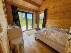 A wooden cabin room with a bed, a desk, and a view of the outdoors. - Charming holiday home near the beach (Gedser)