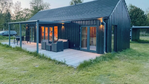 A modern house with a covered patio, large windows, and a deck. - Charming holiday home near the beach (Gedser)