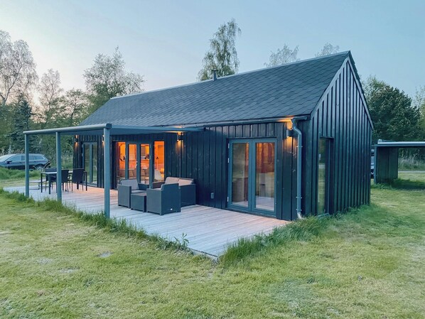 A modern house with a covered patio, large windows, and a deck. - Charming holiday home near the beach (Gedser)
