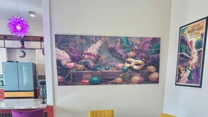 A dining area with a round table and yellow chairs, a purple bar stool, and a wall with a Mardi Gras themed painting. - Main Street House with private pool! (Bay St. Louis)