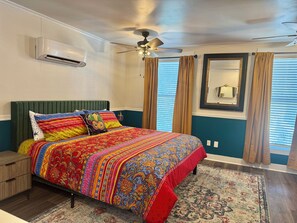 A bedroom with a bed, a ceiling fan, an air conditioning unit, a nightstand, a dresser, and a window with curtains. - Main Street House with private pool! (Bay St. Louis)